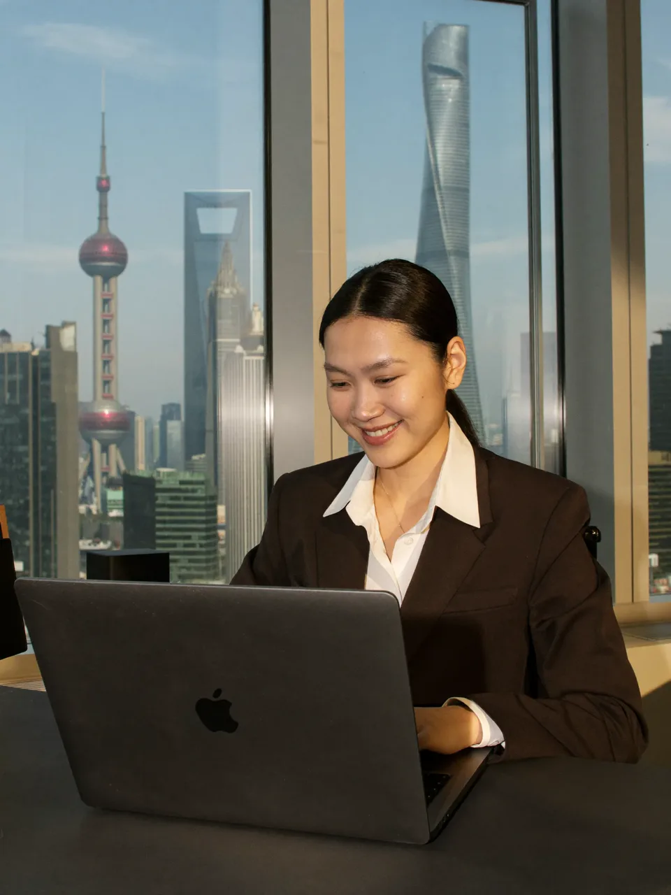 Frau liest die Nachricht am Laptop, hinter ihr die Skyline von Shanghai